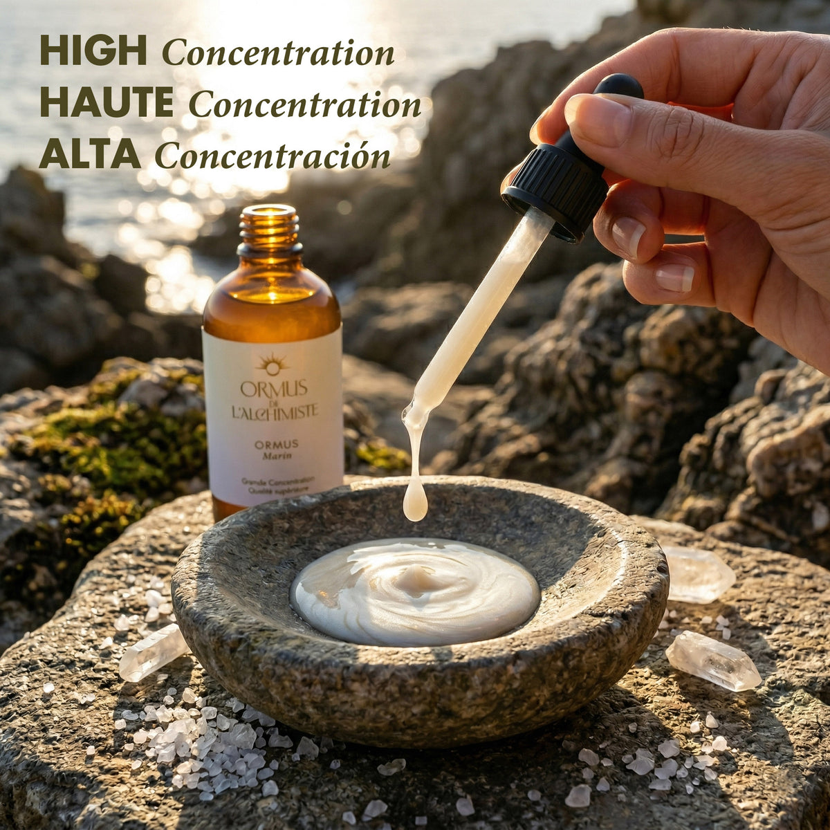 Detailed outdoor presentation of 'ORMUS DE L'ALCHIMISTE' on a sun-drenched Mediterranean rocky coast. A hand uses a pipette to carefully dispense a drop of white, concentrated Ormus into an artisanal stone mortar. Scattered quartz points, coarse sea salt, and the amber product bottle surround the scene. High concentration text is prominent in three languages: 'HIGH Concentration HAUTE Concentration ALTA Concentración'. Golden hour light and sea reflections enhance the spiritual Manna vibration. Premium qual